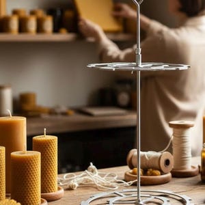 May include: A stainless steel candle making stand with a circular base and top, and a central rod. Several yellow beeswax candles of various sizes are on a wooden table. Spools of thread and other candle-making supplies are also visible.