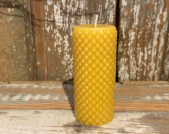 May include: A tall, yellow beeswax candle with a honeycomb pattern. The candle is sitting on a wooden surface.