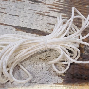 May include: A close-up of a white cotton cord, wound into a coil, on a wooden surface.