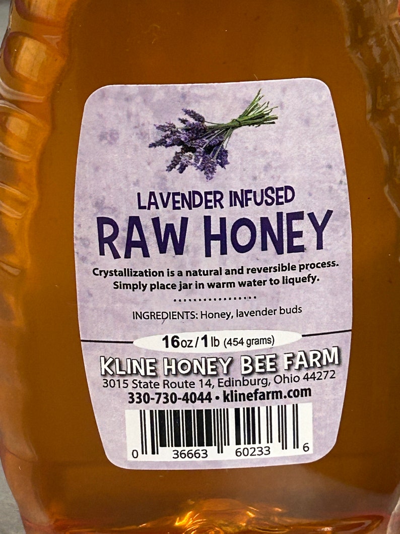 May include: A clear glass bottle of lavender infused raw honey with a white label. The label has a purple and green lavender flower graphic, the text "Lavender Infused Raw Honey", and the ingredients "Honey, lavender buds". The label also includes the brand name "Kline Honey Bee Farm", the address "3015 State Route 14, Edinburg, Ohio 44272", the phone number "330-730-4044", the website "klinefarm.com", and a barcode.