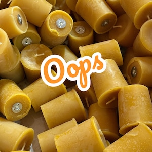 May include: A collection of cylindrical, yellow beeswax candles with wicks and metal inserts. The candles are arranged in a close-up shot, with the word "Oops" in an orange and white design in the lower left corner.