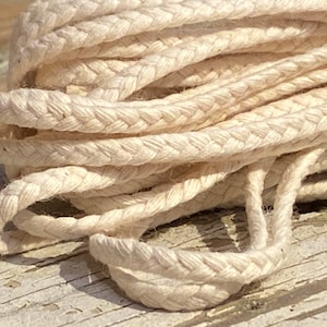 May include: Close-up of a white braided cotton cord. The cord is made of multiple strands of cotton that are woven together to create a strong and durable rope.