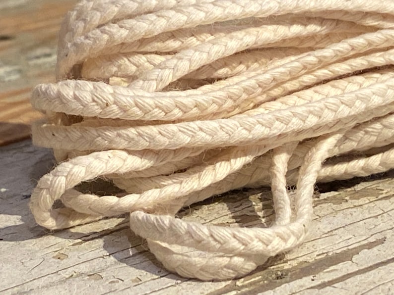 May include: Close-up of a white braided cotton cord. The cord is made of multiple strands of cotton that are woven together to create a strong and durable rope.