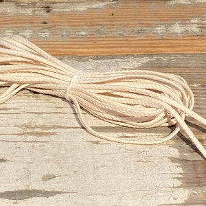May include: A close-up of a coil of natural white cotton cord on a weathered wooden surface.