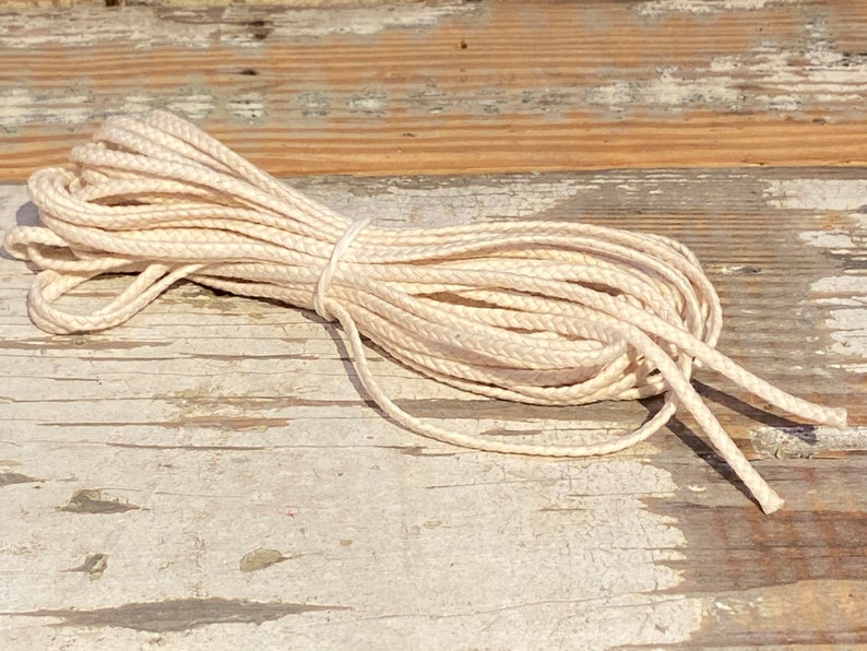 May include: A close-up of a coil of natural white cotton cord on a weathered wooden surface.