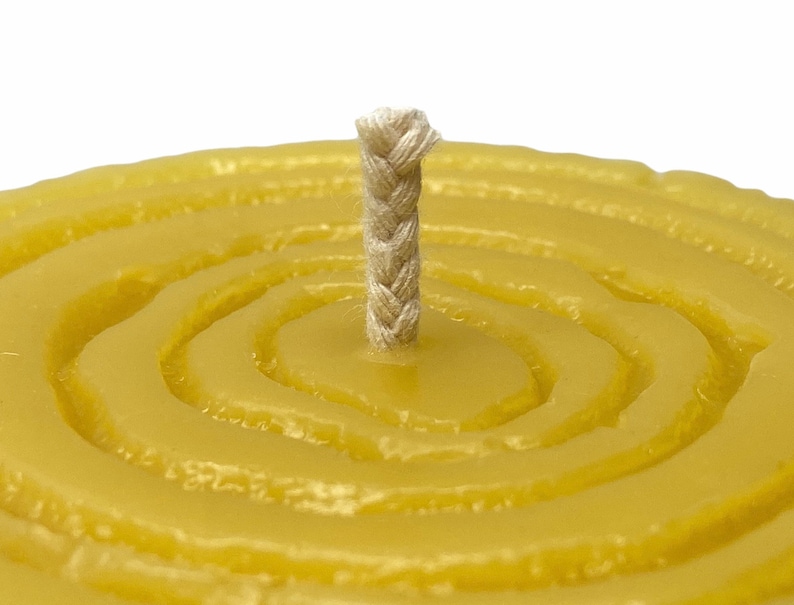 May include: A close-up of a round, yellow beeswax candle with a braided cotton wick in the centre. The candle has a textured, circular pattern.