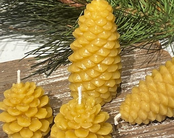 May include: Four yellow beeswax candles shaped like pine cones. The candles are on a wooden surface.