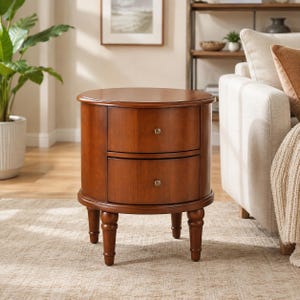May include: A round wooden nightstand with a warm brown finish, featuring two stacked drawers with small, centered metal knobs. The piece is supported by four turned legs that provide a stable base for the cylindrical storage unit.