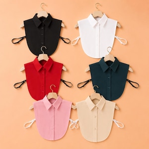 Pode incluir: Uma coleção de seis golas de camisa removíveis em preto, branco, vermelho, verde escuro, rosa claro e bege. Cada gola apresenta um design pontiagudo, uma carcela frontal com botões e tiras laterais elásticas ajustáveis.