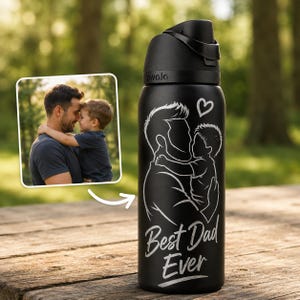 Op de afbeelding: Zwarte waterfles met een klapdeksel. De fles heeft een witte afbeelding van een vader en kind die elkaar omhelzen, met een hart erboven en de woorden "Best Dad Ever" eronder. Op de achtergrond een ingelijste foto van een vader en kind.