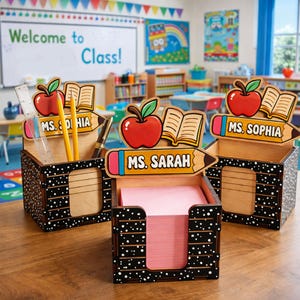 May include: Three wooden desk organizers with a black and white polka dot design. Each features a pencil-shaped nameplate with the names "Ms. Sophia", "Ms. Sarah", and "Ms. Dihia". The organizers have apple and book accents, and hold pencils, a ruler, and pink sticky notes.
