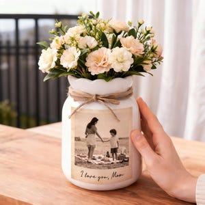 May include: A white ceramic vase with a sepia-toned photograph of a mother and child, tied with twine and filled with peach and cream-colored flowers. The text "I love you, Mom" is printed below the photo.
