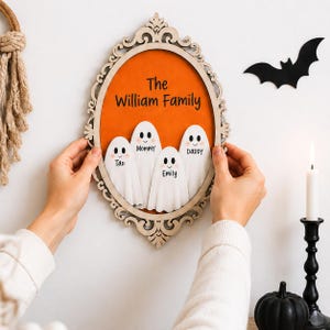 May include: An oval wooden wall plaque with an orange background featuring four white ghost figures. The text reads The William Family, with individual names Mommy, Daddy, Tao, and Emily printed on each ghost. The frame has an ornate, carved design.