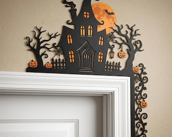 May include: A black laser-cut door corner decoration featuring a haunted house silhouette with orange windows, a full moon with a bat, bare trees, spider webs, and several small orange jack-o'-lanterns arranged along the frame edges.