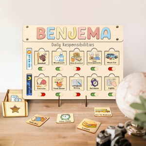 May include: A wooden daily responsibility chart with the name "BENJEMA" at the top. The chart has 12 slots with pictures and text for activities like "Baseball", "Mouthwash", "Make Breakfast", "Visit Grandparents", "Wash Car", "Exercise", "Cook Dinner", "Writing", "Set Alarm", and "Lights". There are also 6 smaller cards with pictures and text for activities like "Make Bed", "Your Time", "Lunch", and "Go To School".