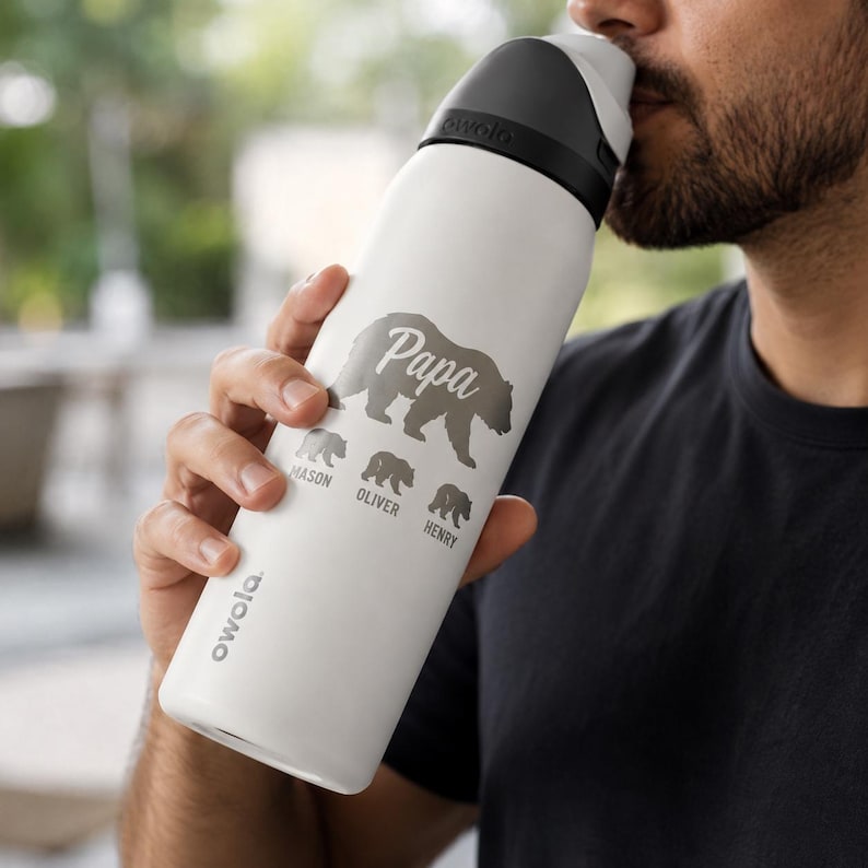 May include: White insulated water bottle with a black lid. The bottle features the word "Papa" above a bear graphic, with the names "Mason", "Oliver", and "Henry" below. The brand name "owala" is printed on the side.