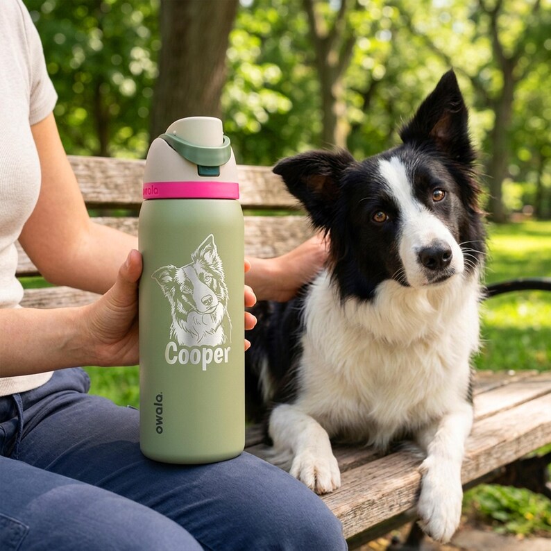Puede incluir: Una botella de agua Owala verde oliva con una banda rosa y un asa verde. La botella presenta un retrato de perro y el nombre "Cooper" en blanco. Un perro Border Collie blanco y negro est&aacute; en el fondo.