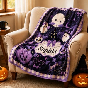 May include: A purple and black patterned throw blanket featuring a central white label with the name Sophia printed in black. The design includes a smiling moon, ghosts, a haunted house, a skull, a black cat, and pumpkins with a checkered border.