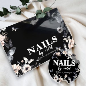 Puede incluir: Caja rectangular negra y posavasos redondo con el texto "NAILS by Adel" en blanco. Ambos art&iacute;culos presentan un dise&ntilde;o floral y de mariposas en tonos blancos, grises y rosas.