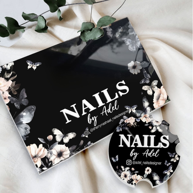 Puede incluir: Caja rectangular negra y posavasos redondo con el texto "NAILS by Adel" en blanco. Ambos art&iacute;culos presentan un dise&ntilde;o floral y de mariposas en tonos blancos, grises y rosas.