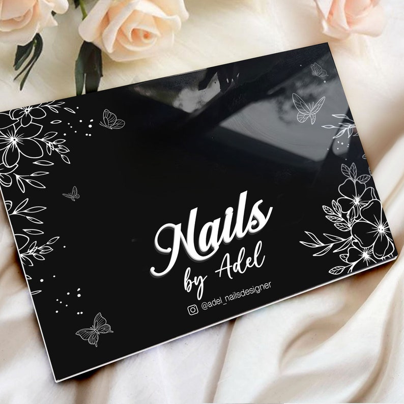 Puede incluir: Paleta rectangular negra para nail art con dise&ntilde;os florales y mariposas blancas. El texto "Nails by Adel" se muestra en una fuente elegante. Tambi&eacute;n es visible el identificador de Instagram "@adel_nailsdesigner".