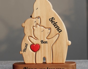 Puede incluir: Figura de madera de una familia de osos con los nombres Selena, Hazel y Ben grabados en ella. Los osos se abrazan y tienen un corazón rojo en el medio. La base de la figura tiene el texto "Nana, we love you" grabado.