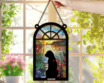 May include: A stained glass window hanging with a black silhouette of a dog sitting in a field of flowers. The window has a sunset scene with a lake and trees. The text "Cupper" is at the bottom of the window.