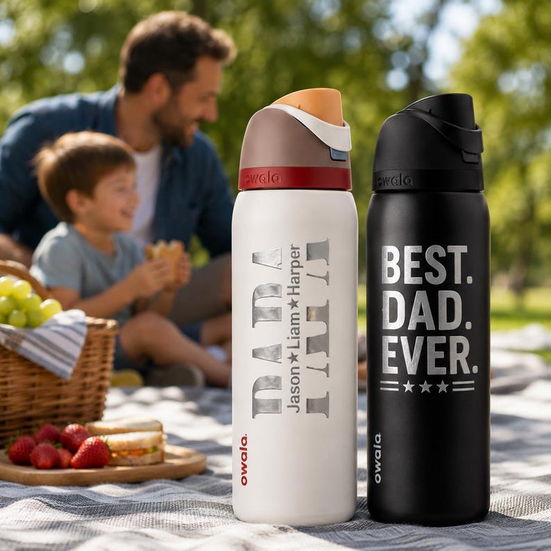 May include: Two insulated water bottles. One is white with "DADA" and "Jason Liam Harper" printed on it. The other is black with "BEST. DAD. EVER." printed on it. Both have a black lid and are designed for outdoor use.