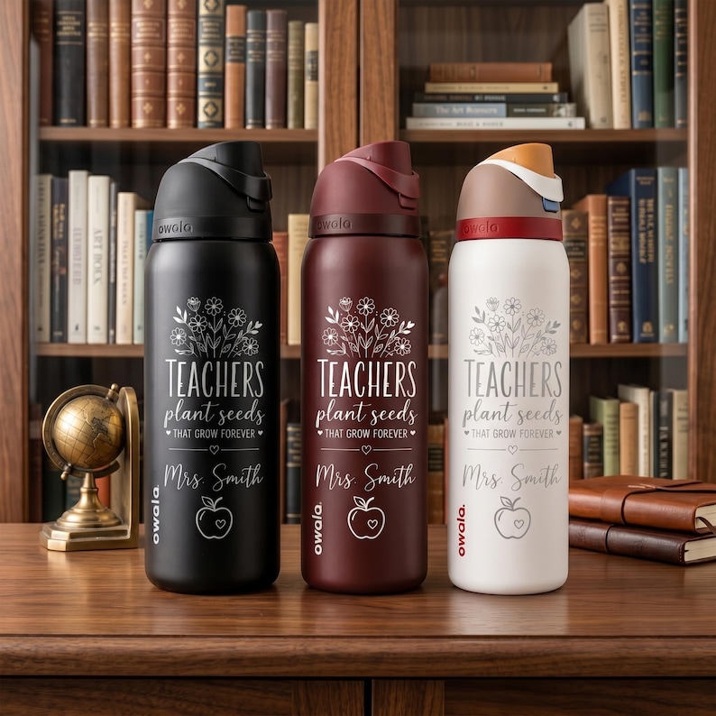 May include: Three insulated water bottles in black, burgundy, and white. Each bottle has a floral design and the text "TEACHERS plant seeds THAT GROW FOREVER" with "Mrs. Smith" and an apple graphic. The bottles are on a wooden surface.