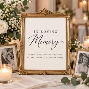 May include: A gold ornate picture frame containing a white sign with black text that reads: IN LOVING Memory OF THOSE WHO CANNOT BE HERE TODAY BUT ARE FOREVER PRESENT IN OUR HEARTS. The frame features intricate scrollwork and a decorative top crest.