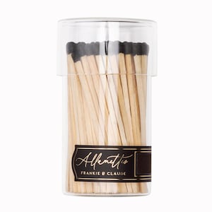 May include: A glass jar filled with wooden matches with black tips. The jar has a black label with gold lettering that reads "Alfenito's Frankie & Claude".