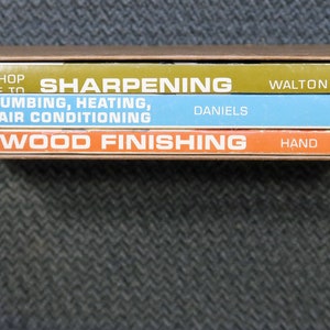 May include: A set of three vintage books in a brown cardboard box. The book titles include "Sharpening", "Plumbing, Heating, Air Conditioning", and "Wood Finishing". The books are in various colors, including green, blue, and orange.