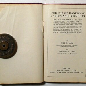 May include: A book titled "The Use of Handbook Tables and Formulas" by John M. Amiss and Franklin D. Jones. The book cover is white with black text and is open to the title page. The book is on a red surface.