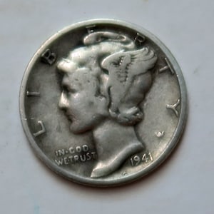 May include: A silver 1941 Mercury dime coin with the profile of Liberty on the obverse side. The coin has the inscription "IN GOD WE TRUST" and the year "1941".