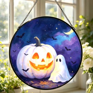 May include: A circular suncatcher featuring a painted scene of a glowing orange jack-o'-lantern and a white ghost against a dark purple and blue night sky with bats, stars, and a crescent moon, suspended by a black metal chain.