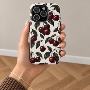 Peut inclure: Une coque de smartphone avec un motif répétitif de cerises rouge foncé et de feuilles vertes sur fond blanc. La coque présente une découpe noire pour l'appareil photo en haut à gauche, illustrant un motif botanique de fruits.