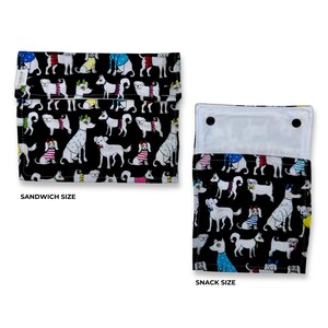Peut inclure: Deux sacs alimentaires en tissu réutilisables avec un fond noir présentant un motif répétitif de chiens blancs portant des accessoires colorés. Le sac de gauche est marqué SANDWICH SIZE et celui de droite SNACK SIZE, avec une doublure blanche.