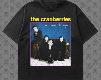 May include: A black short-sleeve t-shirt featuring a graphic print of the band The Cranberries. The print displays the text "the cranberries" in yellow and "no need to argue" in white, with a photograph of the band members on a couch.