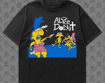 May include: A black short-sleeve t-shirt featuring a graphic print with the text ALICE DONUT. The illustration depicts yellow cartoon figures, one with blue hair holding a small white object and a gun, against a blue ground.