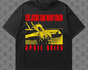 May include: A black short-sleeve t-shirt featuring a yellow graphic of a figure with arms outstretched. The text "THE JESUS AND MARY CHAIN" appears in red above the graphic, and the text "APRIL SKIES" appears in red below the graphic.