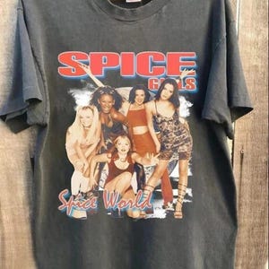 May include: A charcoal gray short-sleeve t-shirt featuring a graphic print of the Spice Girls. The text "SPICE GIRLS" appears in red at the top, and "Spice World" is written in red script at the bottom. The image shows five individuals.