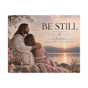 Puede incluir: Un rompecabezas con un paisaje al atardecer donde una persona con túnica blanca se sienta junto a otra envuelta en una manta rosa. El texto dice BE STILL PSALM 46:10 Grace AND KNOW THAT I AM GOD, con un pequeño icono de corazón sobre Grace.