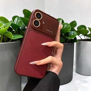 May include: A dark red smartphone case with a textured back panel and a smooth camera housing featuring two circular lenses with gold-toned rims. The text CASE AITO is printed in small white letters on the upper right side of the camera module.