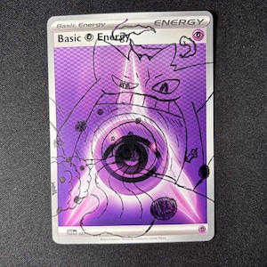May include: A purple Psychic Basic Energy trading card featuring a hand-drawn black ink illustration of a Gengar character over the original card art. The card includes the text Basic Energy, the Psychic energy symbol, and the code SVE 021.