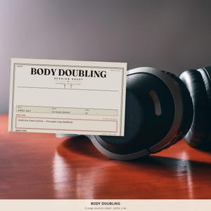 May include: A cream-colored Body Doubling Session Sheet paper form with black text and red accents, featuring fields for date, buddy, time, and main task, positioned in front of black over-ear headphones. The form includes the text Body Doubling.