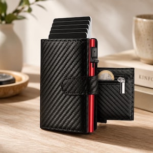 May include: A black carbon fiber textured card holder wallet with a red metallic side panel and a mechanical card ejection trigger. The wallet features a fold-out section with a small zippered pocket containing a one euro coin and multiple black cards.
