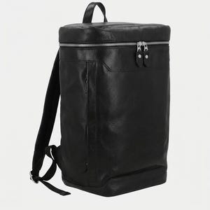 Può includere: Uno zaino in pelle nera dalla silhouette rettangolare, dotato di manico superiore, spallacci regolabili e chiusura con cerniera in metallo argentato sulla parte superiore. Il design include una tasca laterale verticale con cerniera.