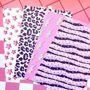 May include: Four rectangular sheets of patterned paper. The first features pink stars on white. The second has a purple and white leopard print. The third is light pink with white polka-dot lightning bolts. The fourth has wavy purple stripes with tiny white stars.