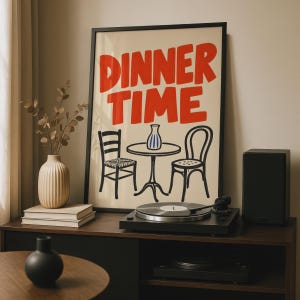 Peut inclure: Une affiche encadrée représentant le texte DINNER TIME en lettres rouges grasses au-dessus d'un dessin au trait noir d'une petite table ronde avec un vase et deux chaises. Le fond de l'affiche est de couleur crème, dans un cadre noir.