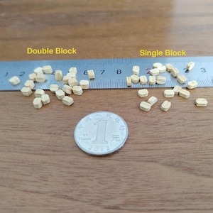 May include: Small light-colored wooden pieces labeled Double Block and Single Block arranged near a metal ruler with centimeter markings and a silver 1 Yuan coin for scale. The wooden pieces are oval-shaped with a central groove, showing their size.